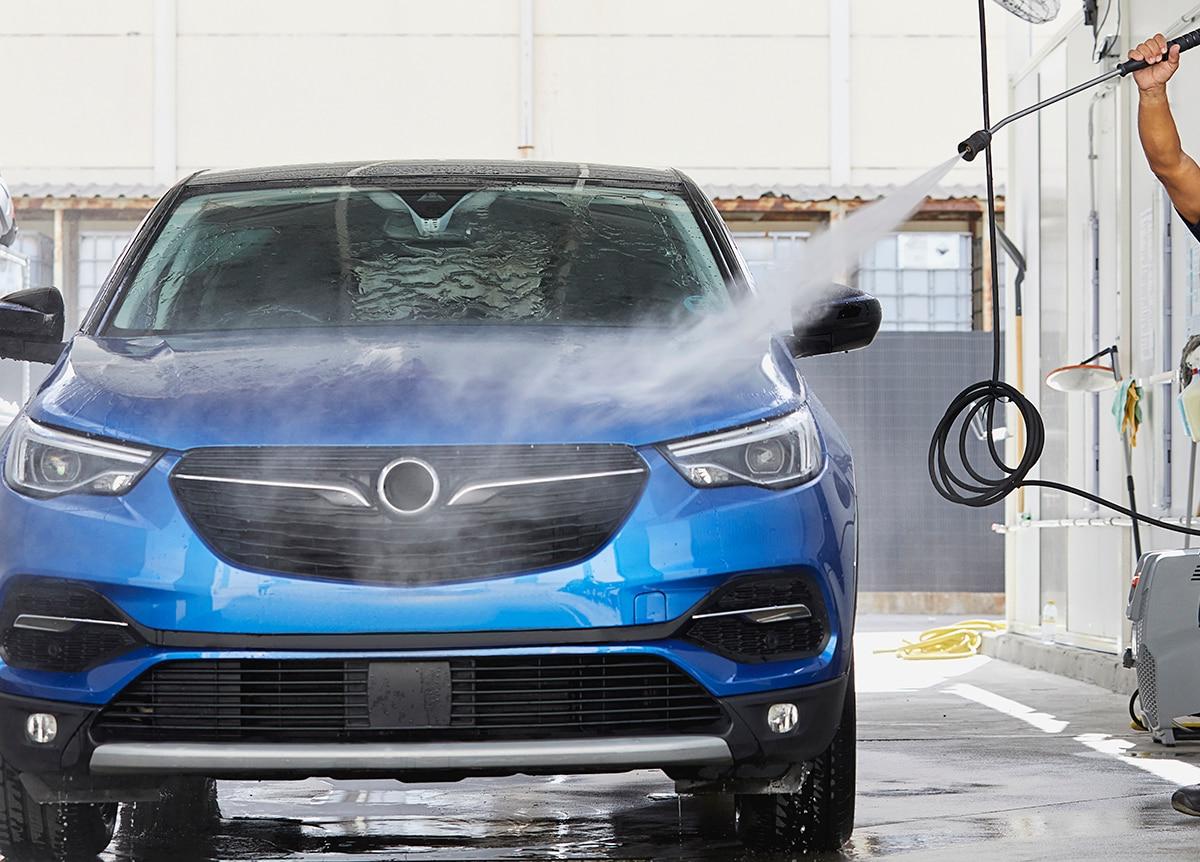 一名企业员工在一辆蓝色汽车的前部喷水.